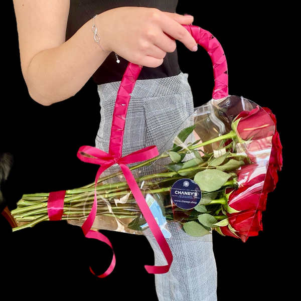 A hand holds a bouquet of red roses wrapped in clear plastic with a pink ribbon.