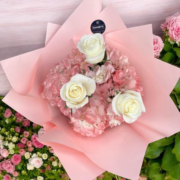 Pink hydrangea bouquet with three white roses wrapped in pale pink paper.