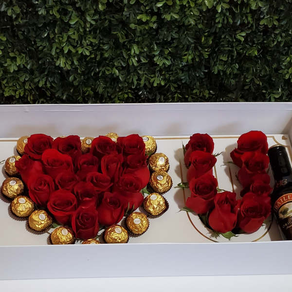 Red roses arranged with chocolates and a Baileys bottle in a gift box