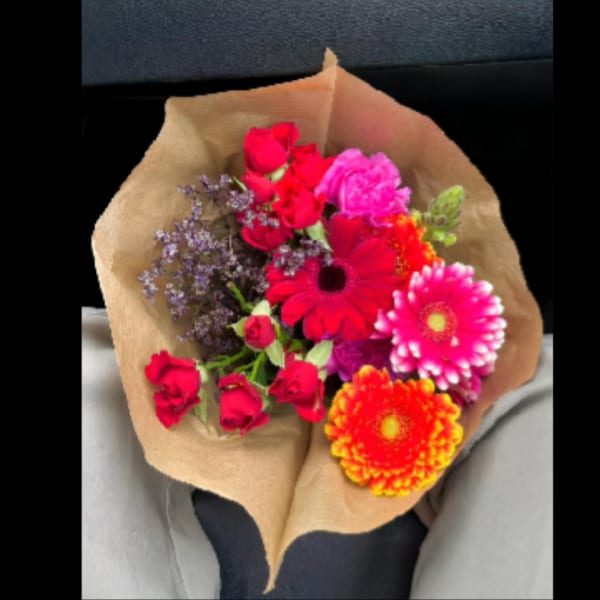 Mixed bouquet of red, pink, and orange flowers wrapped in brown paper