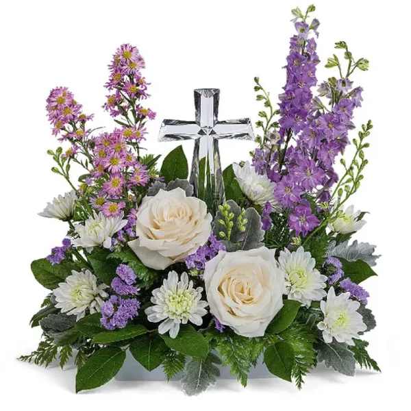 White roses and purple flowers arranged around a clear glass cross