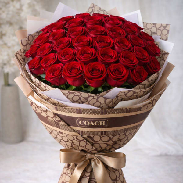 Large bouquet of red roses wrapped in patterned paper with a gold ribbon