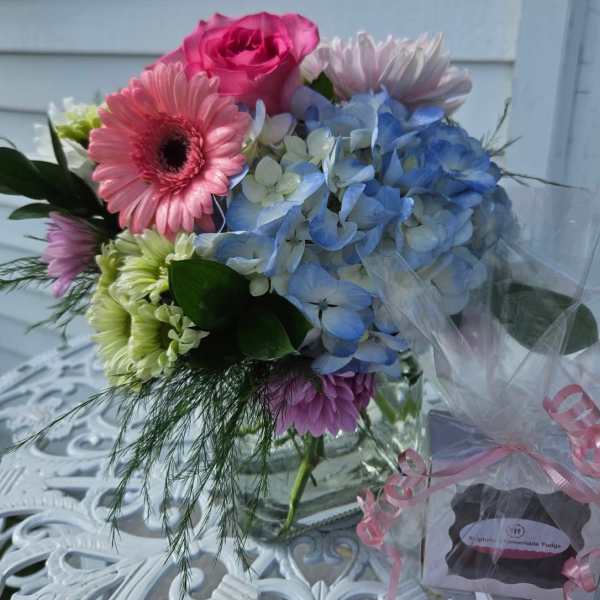 Mixed bouquet with pink gerbera daisies, blue hydrangea, and roses in a glass vase
