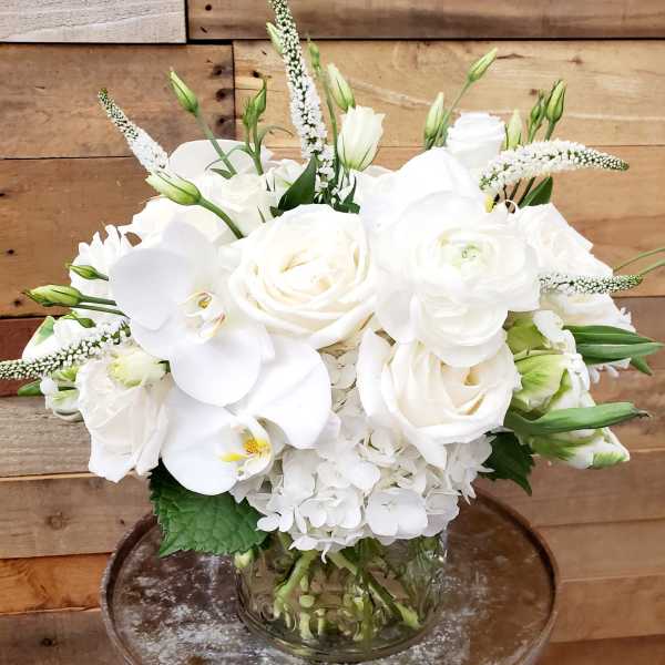 White roses and orchids arranged in a clear glass vase