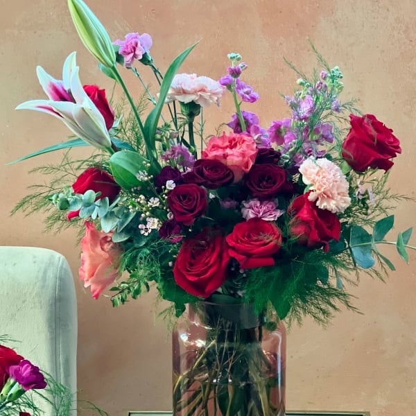 Mixed bouquet of red roses, lilies, and pink carnations in a glass vase