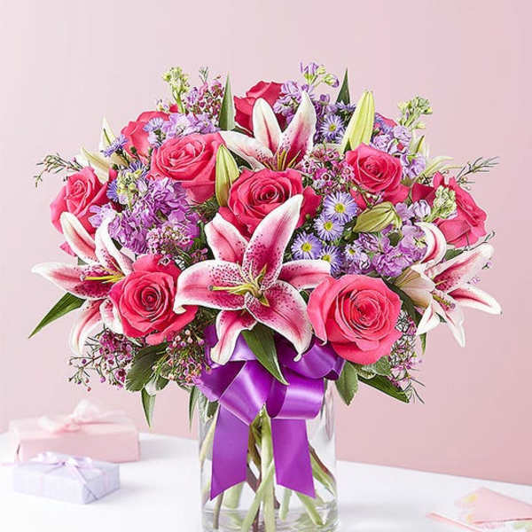 Pink roses and lilies in a glass vase with a purple ribbon
