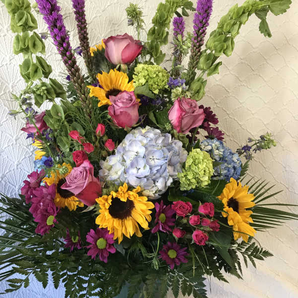 Mixed bouquet with sunflowers, roses, hydrangea, and purple spikes in a vase