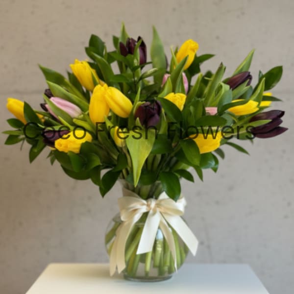 Bouquet of yellow and purple tulips in a glass vase with a ribbon