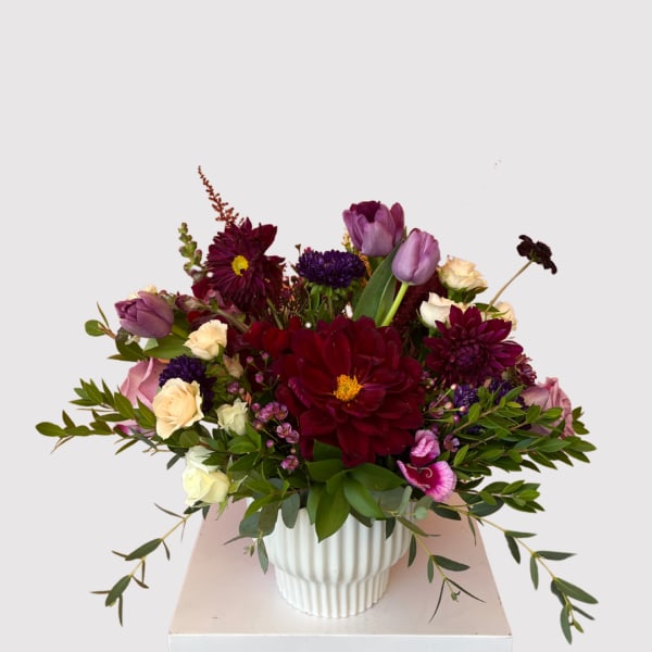 Mixed bouquet of burgundy, purple, and cream flowers in a white vase