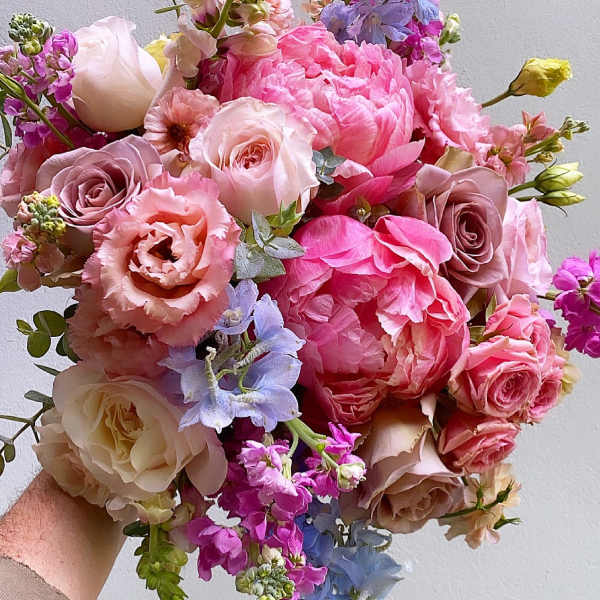 Handheld bouquet of pink and blush roses with peonies and small purple flowers
