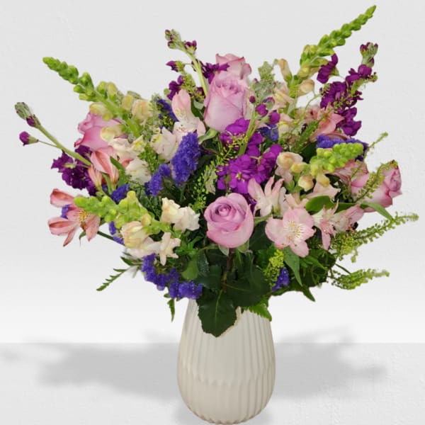 Tall arrangement of pink roses, alstroemeria, and purple flowers in a white ribbed ceramic vase