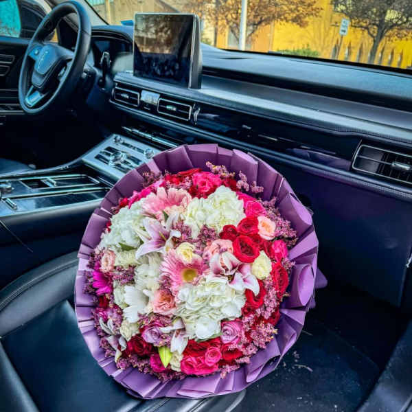 Large bouquet of pink, white, and red flowers wrapped in purple paper