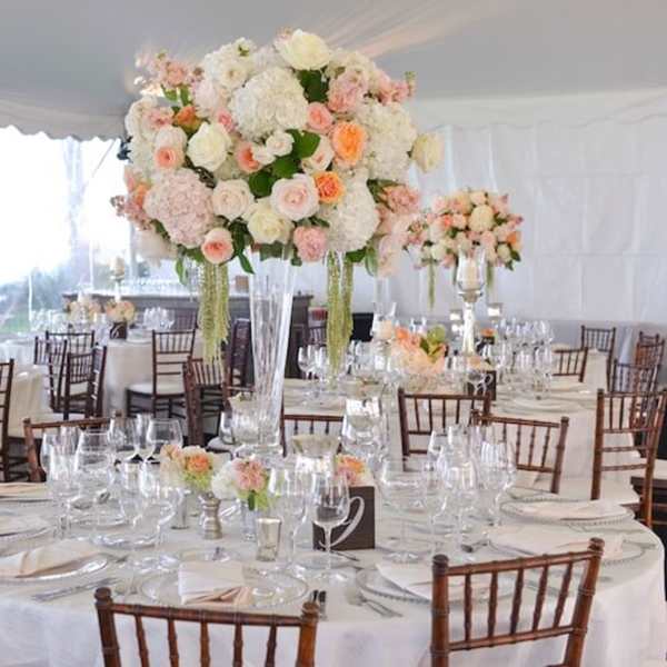 Tall pastel floral centerpieces on round banquet tables in a tented reception