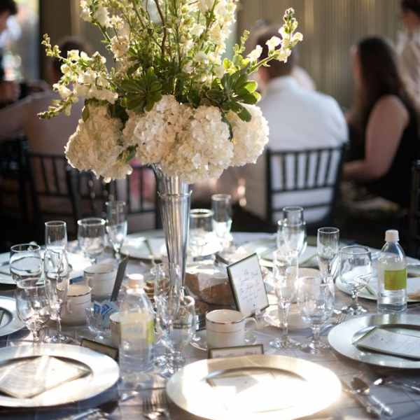 Tall white floral centerpiece in a silver vase on a set dining table