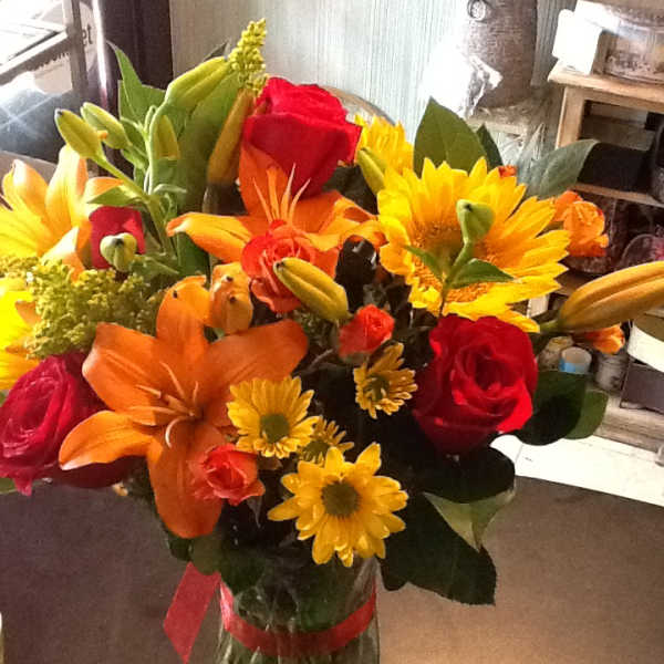 Bouquet of red roses, orange lilies, and yellow daisies in a glass vase