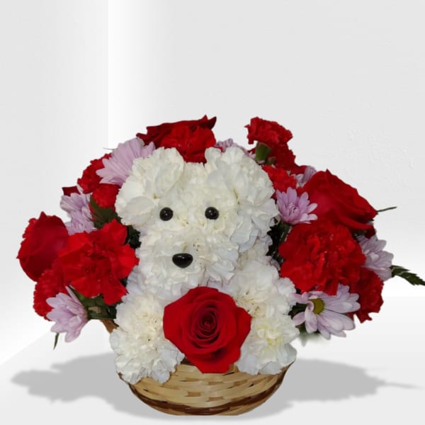 Basket arrangement with a white carnation dog surrounded by red roses and carnations