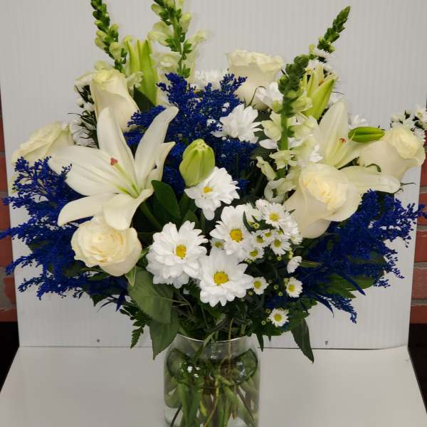 Tall vase arrangement of white lilies, roses, and daisies with bright blue filler flowers