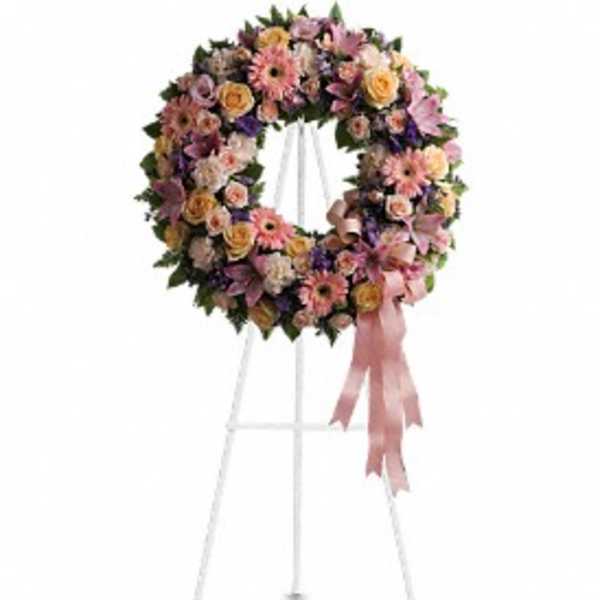 Pastel standing wreath of pink lilies, roses, and gerbera daisies on a white easel with a pink ribbon