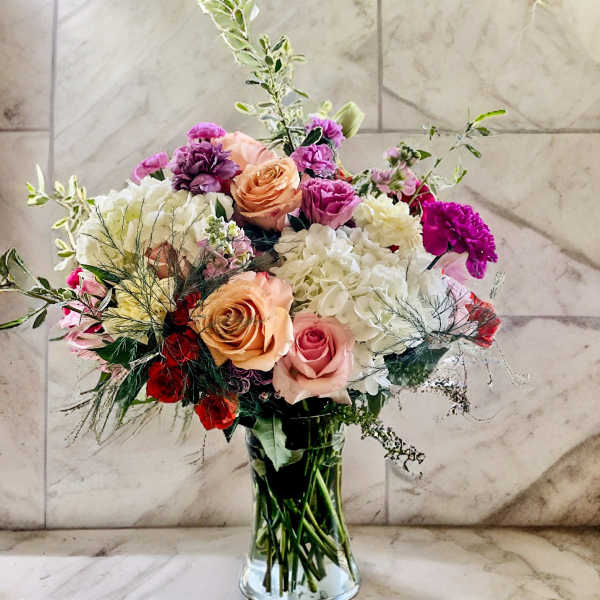 Mixed bouquet of roses, hydrangeas, and carnations in a glass vase
