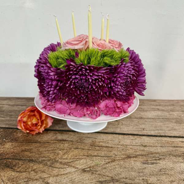 Pink and purple floral cake with candles on a white stand