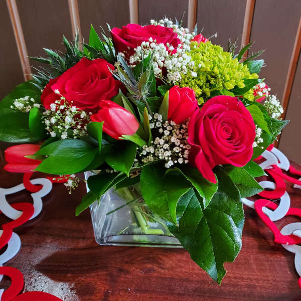 Red roses and pink tulips in a glass vase with white filler flowers