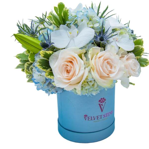 Blue and white floral arrangement in a blue hatbox with roses and orchids