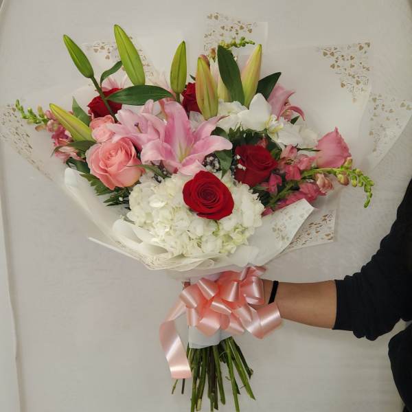 Hand-tied bouquet of pink lilies, roses, and white hydrangeas wrapped with pink ribbon.