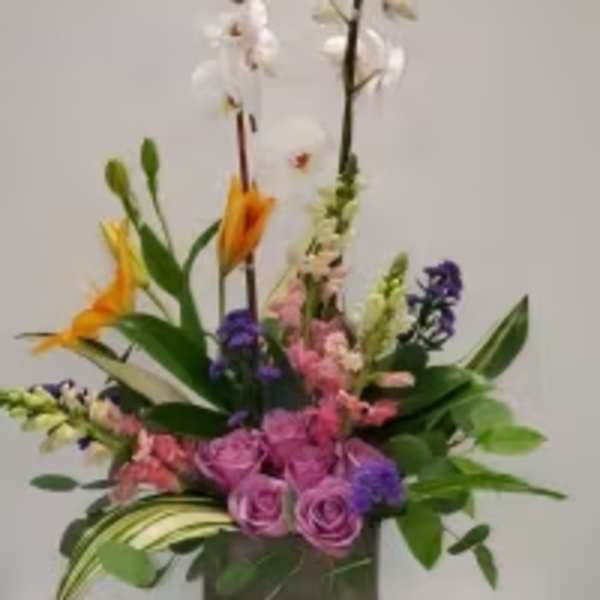Tall mixed floral arrangement in a dark square vase with pink, purple, white, and orange blooms