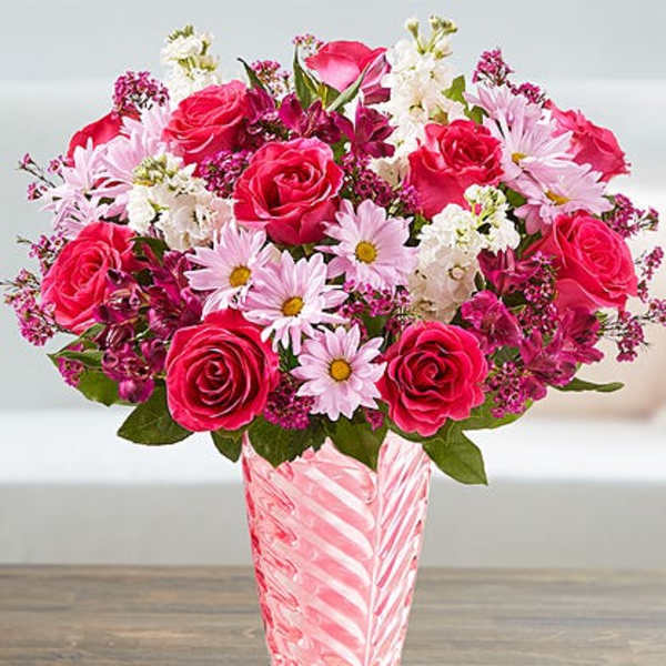 Pink and white mixed bouquet with roses and daisies in a tall pink glass vase