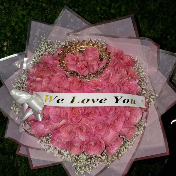 Round bouquet of pink roses with baby’s breath, crown accent, and a ‘We Love You’ banner.