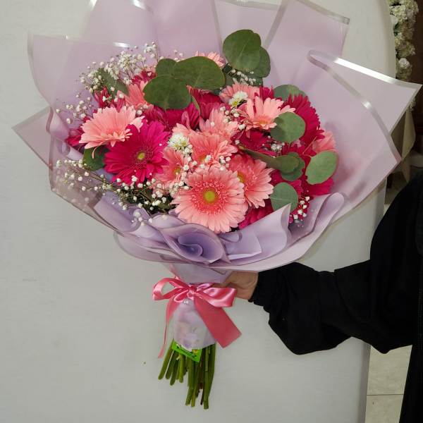 Hand-tied bouquet of pink gerbera daisies wrapped in lavender paper with a pink ribbon bow