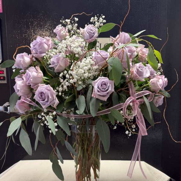 Lavender roses in a clear glass vase with baby's breath and ribbon