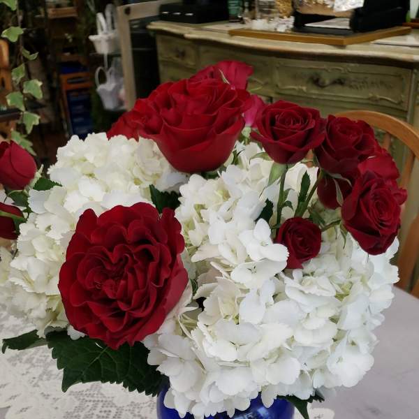 Red roses and white hydrangeas arranged in a blue glass vase on a lace table runner