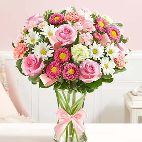 Pink roses and daisies arranged in a clear glass vase with a pink ribbon