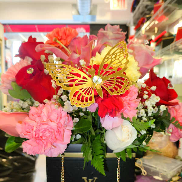 Mixed pink and red flower arrangement in a black box with a gold butterfly