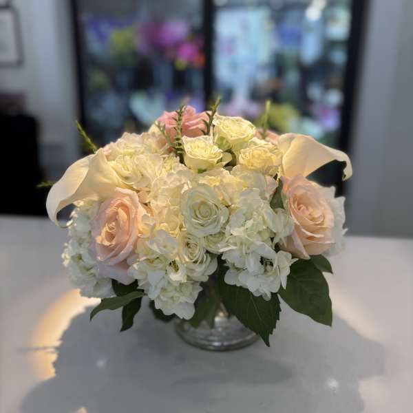 Cream and blush rose bouquet with white hydrangeas in a glass vase