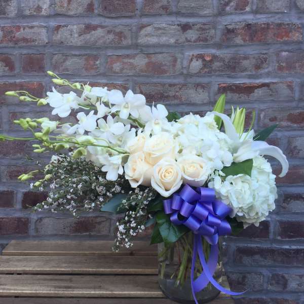 White floral arrangement in a glass vase with a purple ribbon