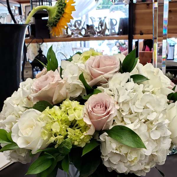 Low arrangement of white hydrangeas and blush roses in a clear glass cube vase