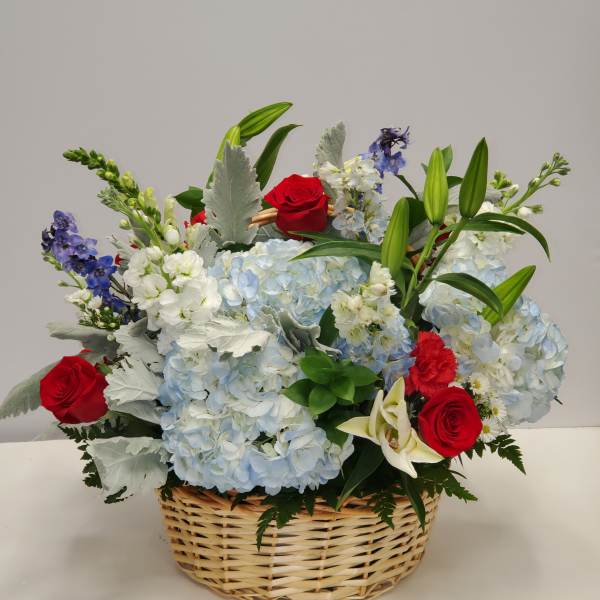 Basket arrangement with blue hydrangeas, red roses, white lilies, and mixed accent flowers