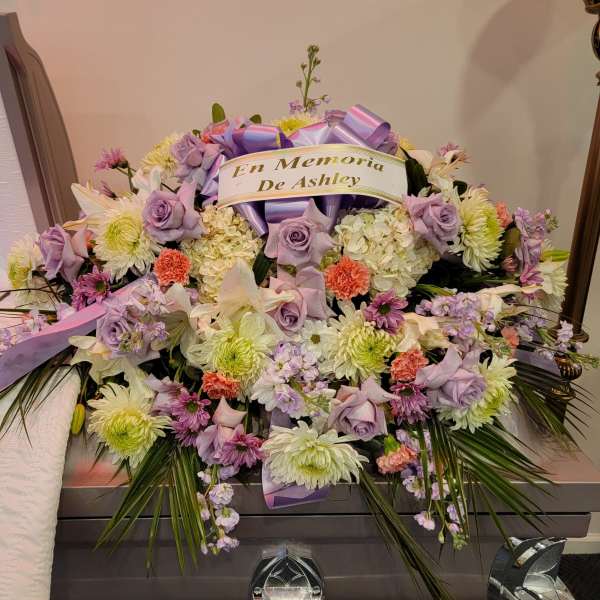 Casket spray of lavender roses, white mums, and mixed blooms with a memorial ribbon