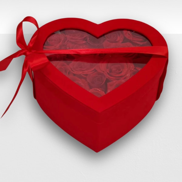 Heart-shaped red box filled with red roses under a clear lid and tied with a red ribbon