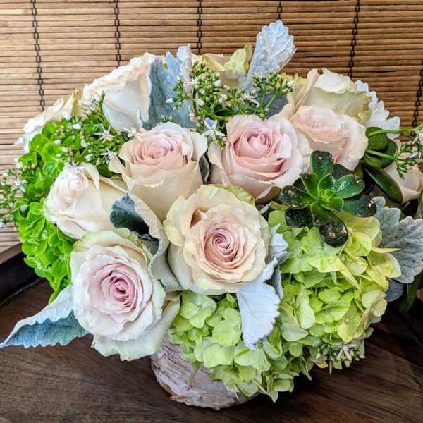 Low arrangement of blush roses, green hydrangeas, and succulents in a rustic container