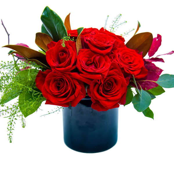 Red roses arranged in a dark blue vase with mixed greenery
