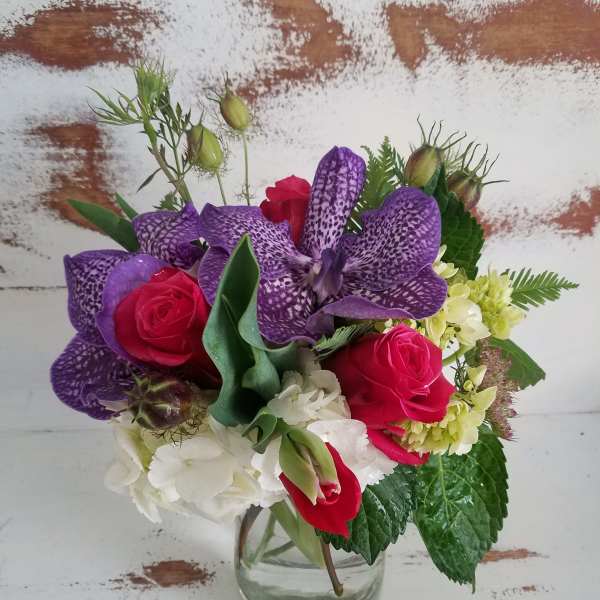 Bouquet of purple orchids, red roses, and white hydrangea in a clear glass vase