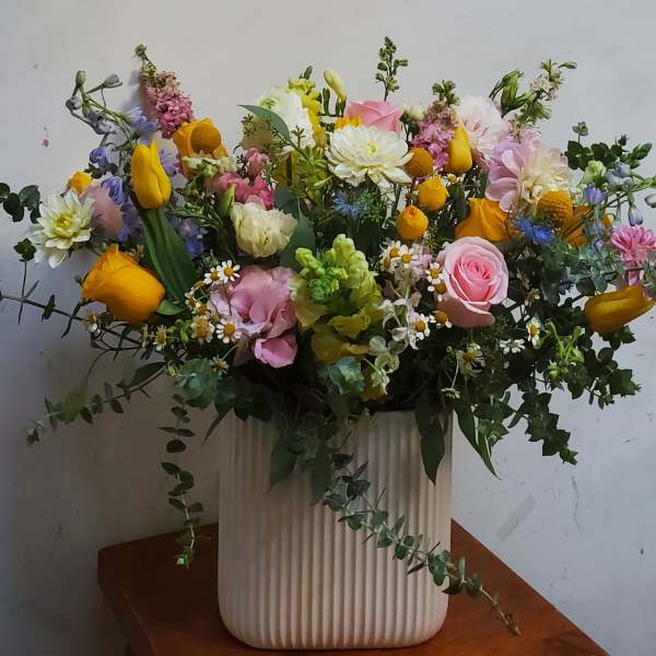 Mixed bouquet in a ribbed white vase with pink, yellow, and white flowers