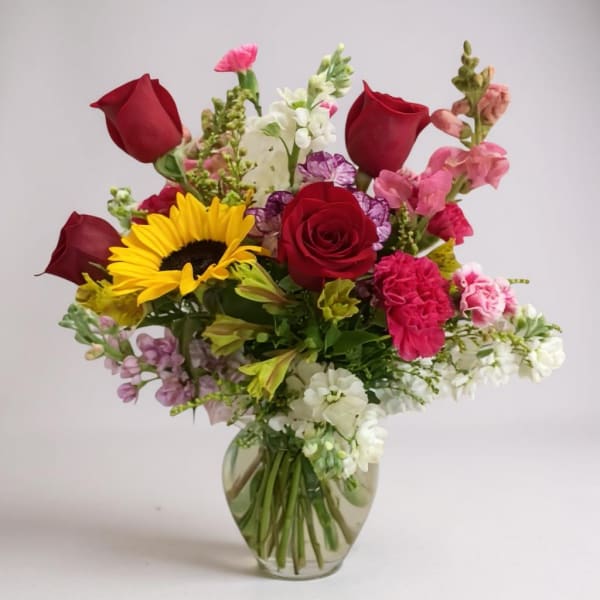 Mixed bouquet with red roses, a sunflower, and pink blooms in a glass vase