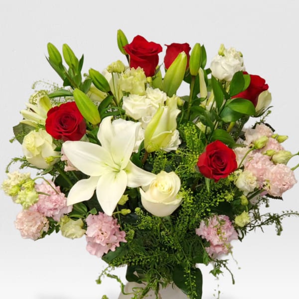 Tall arrangement of red roses, white lilies, and mixed pastel blooms in a white vase