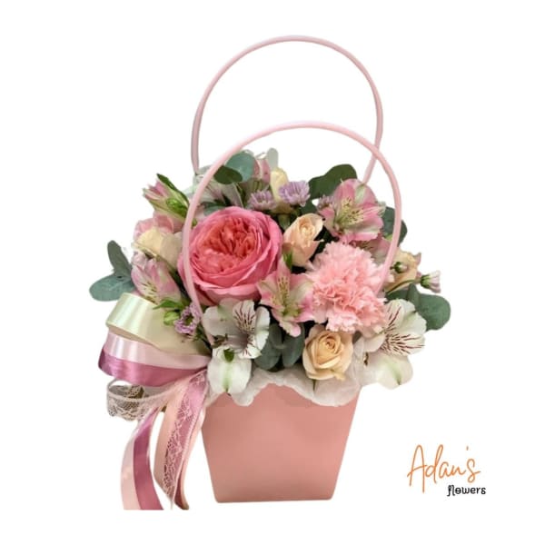 Pink floral arrangement in a pastel basket with ribbon handles
