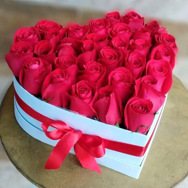 Heart-shaped box filled with bright pink roses and tied with a red ribbon