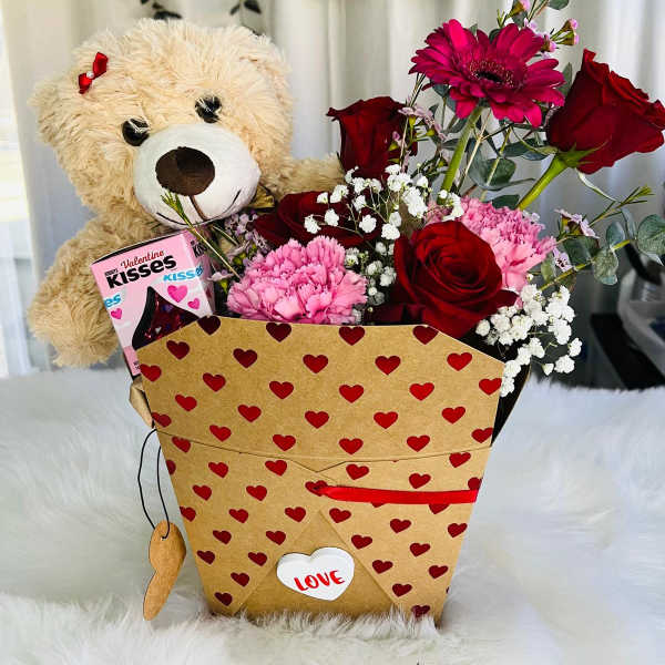 Teddy bear and red flower arrangement in a heart-patterned gift box